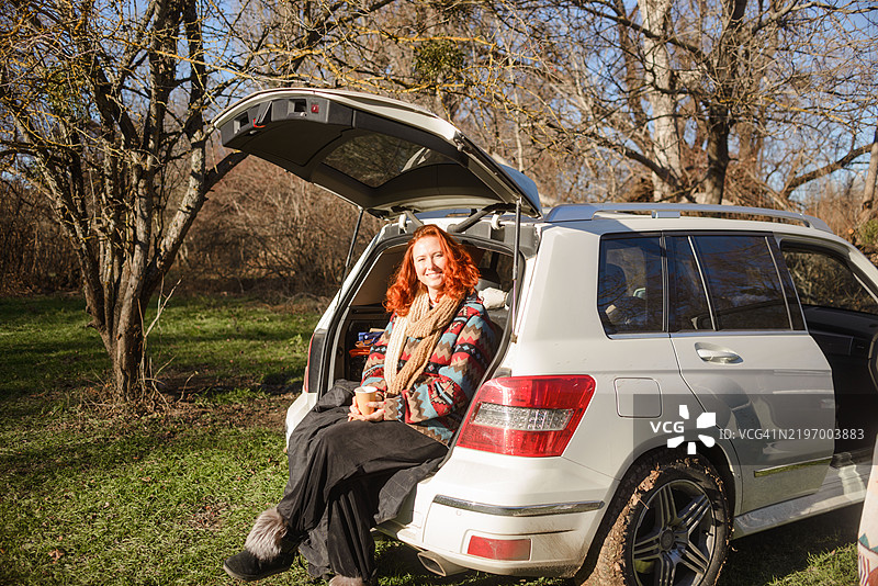 在自然环境中，女人悠闲地坐在敞开的汽车后备厢里图片素材