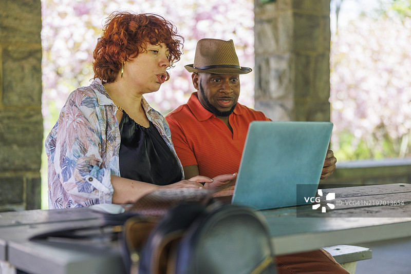 成熟的自由职业者在公园工作。跨种族情侣在新泽西州麦迪逊的詹姆斯公园春季使用笔记本电脑进行远程工作。图片素材
