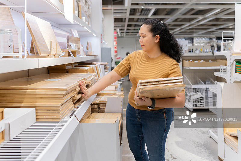 亚洲中年小企业主在商店货架上整理木质切菜板图片素材