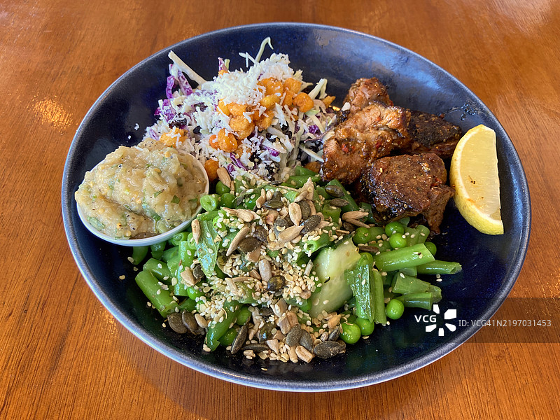 调味腌制鸡肉的碗；配有剁碎的哈卢米奶酪、红卷心菜、脆玉米、黑加仑、新鲜香草、大蒜蛋黄酱的凉拌菜；青豆和豌豆、黄瓜、薄荷，顶部撒上南瓜子、芝麻和葵花籽混合；以及烟熏茄子酱。图片素材