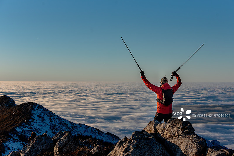 登山者在日出时站在云层之上的山峰上图片素材