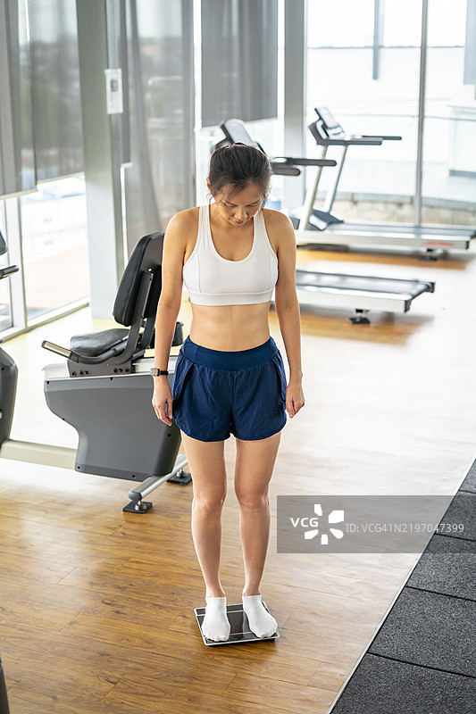 女性在健身房的体重秤上站着图片素材