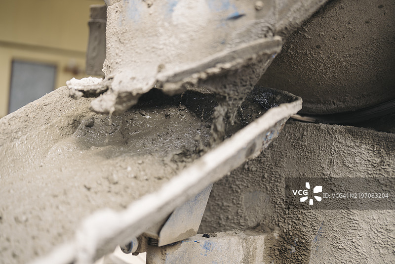 一辆覆盖着干混凝土的混凝土搅拌车的细节视图，展示了其旋转的搅拌筒、料斗和工业设计，位于建筑工地上。图片素材