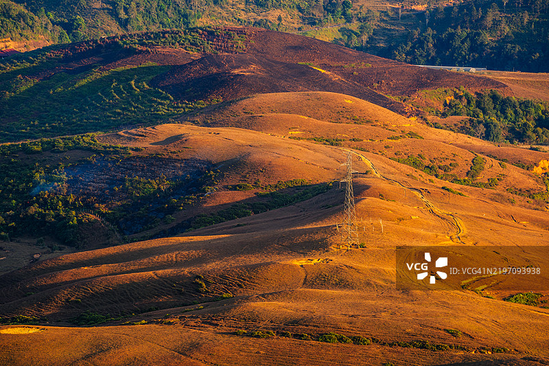 一根信号天线矗立在起伏的金色山丘上，沐浴在温暖的日落光线中，周围是干燥的植被和迷人的风景。图片素材