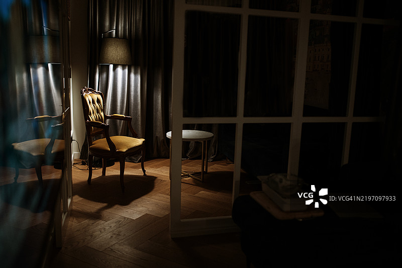 透过玻璃门可以看到一个昏暗的房间，里面有一把椅子和一盏灯。这个场景传达出一种安静、舒适和私密空间的感觉，伴随着柔和的灯光。图片素材