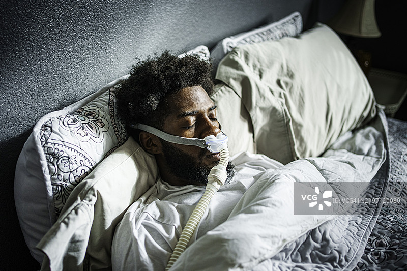 年轻的非裔美国男子，二十多岁，安静地使用CPAP机睡眠以治疗睡眠呼吸暂停。图片素材