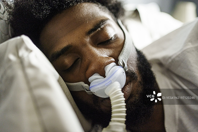 年轻的非裔美国男子，二十多岁，安静地使用CPAP机睡眠以治疗睡眠呼吸暂停。图片素材