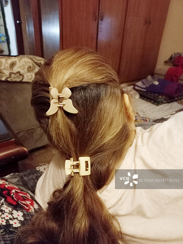 成熟的女性在凌乱的客厅中放松，后视图显示她的双色染发马尾辫用发夹扎起。图片素材