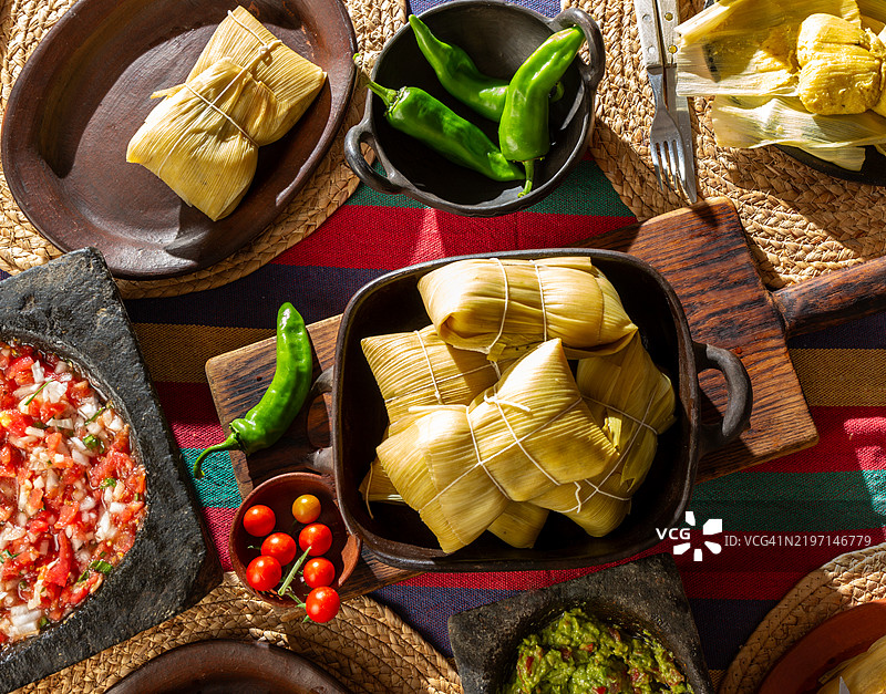 传统智利玉米饺子 - Humitas，一道用玉米面团包裹在玉米皮中的菜肴，配有新鲜番茄酱和石臼捣制的鳄梨酱。图片素材