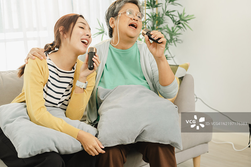 家庭欢乐时光：两位女性在家享受卡拉OK，分享欢笑和温馨的时刻，度过一个舒适的下午。图片素材