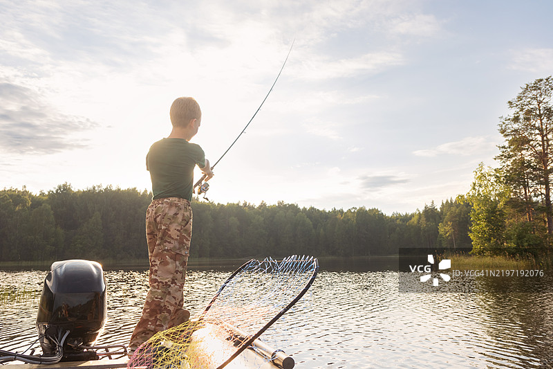 男孩在日落时分从充气摩托艇上钓鱼 - 在森林湖泊中抛竿图片素材