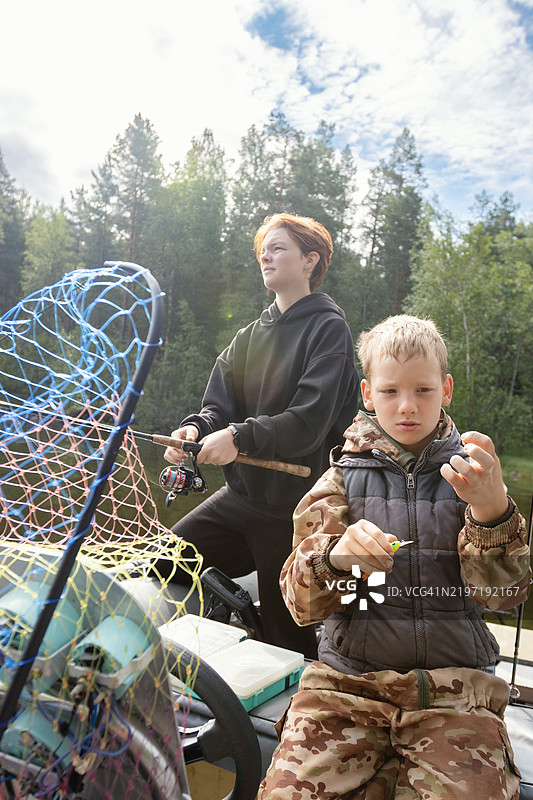 姐妹和兄弟在森林湖泊中从充气摩托艇上钓鱼图片素材