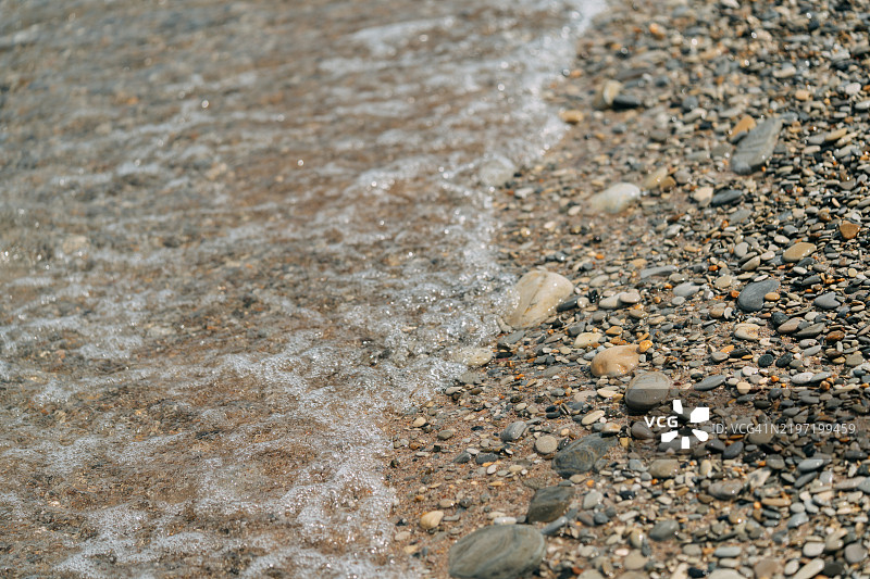 温暖阳光下，温柔的海浪拍打着沙滩上的卵石图片素材