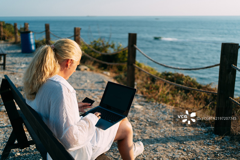 海边的女商人使用笔记本电脑和信用卡在线购物图片素材