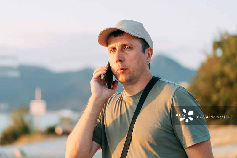 穿着卡其色帽子的游客在海滩上打电话图片素材