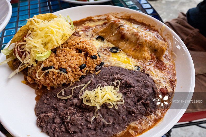 一盘墨西哥菜，包括塔可、碎奶酪、炒豆和淋上酱汁的奶酪卷饼。图片素材