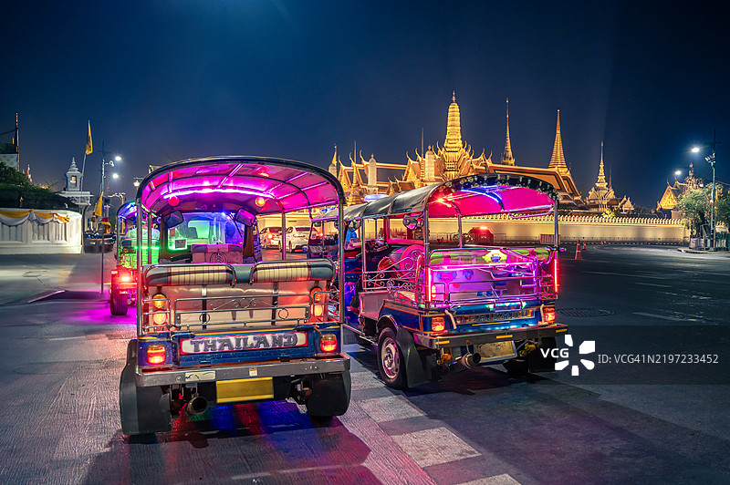 泰国曼谷,2025年1月23日,夜晚的曼谷市中心,一辆装饰华丽的嘟嘟车停在玉佛寺(Wat Phra Kaew)和帕色里拉特那萨萨达拉姆寺(Wat Phra Sri Rattana Satsadaram)前。图片素材