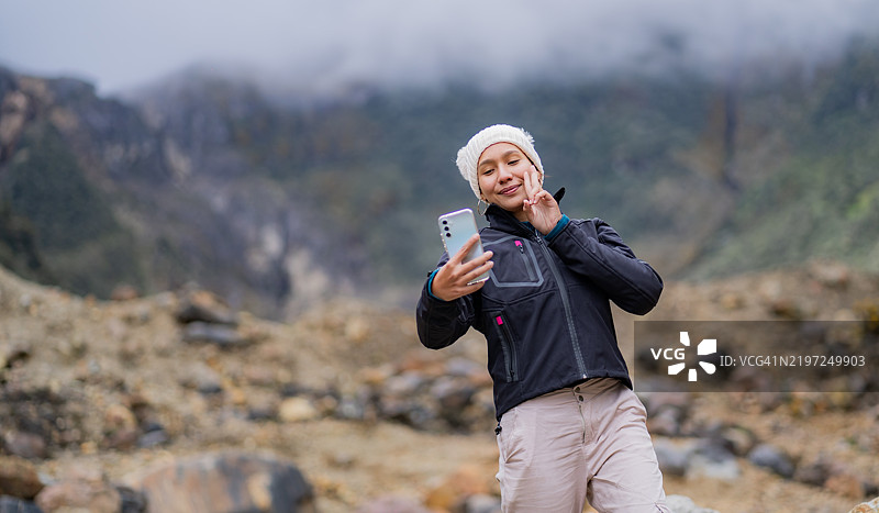 年轻女性站在山上，背景是岩石景观，自拍照。图片素材