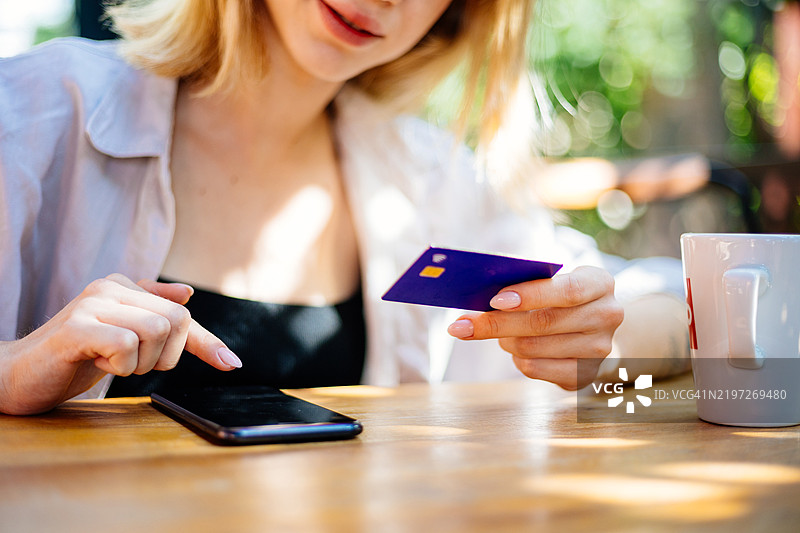 快乐的女性在休息室使用手机进行在线购物，输入信用卡信息，涉及金融科技网站和数字支付。微笑的女性在咖啡馆使用电子商务、零售折扣和银行应用。图片素材