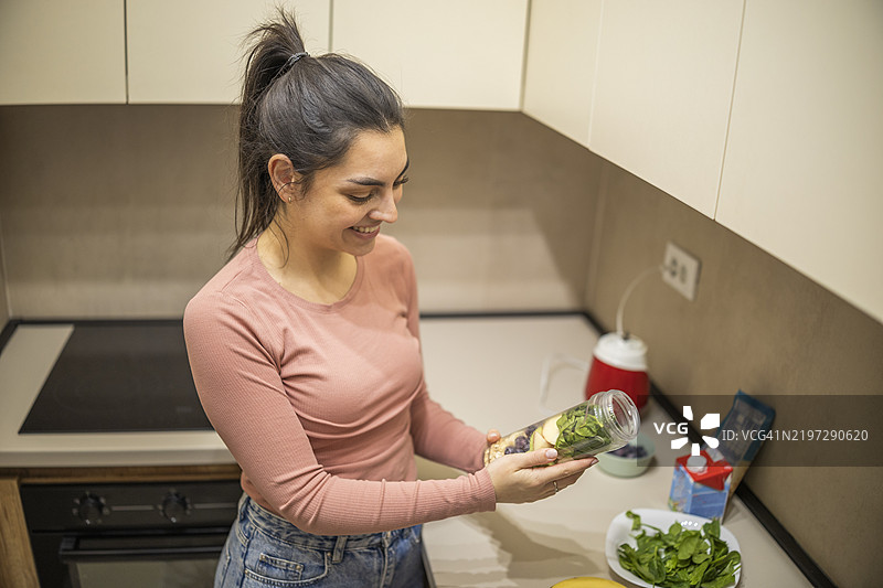 可爱的女性正在看着她放入搅拌杯中的滤网，准备制作健康餐。图片素材