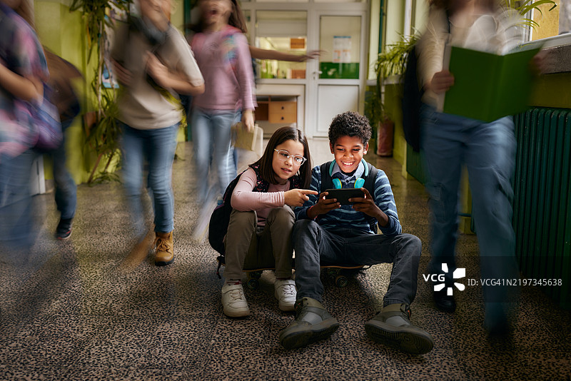 快乐的学生在小学走廊里使用智能手机。图片素材
