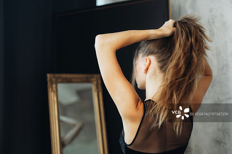 年轻女性穿着黑色连衣裙，在镜子前整理头发。图片素材