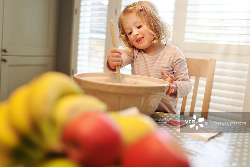 可爱的4岁女孩在家里的厨房里享受着搅拌蛋糕的乐趣。图片素材