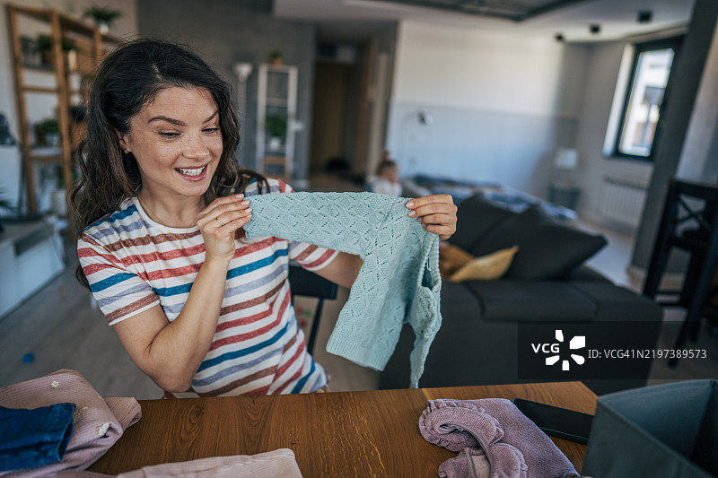 母亲坐在光线明亮的房间里，微笑着在笔记本电脑前展示她为小女儿购买的物品。图片素材