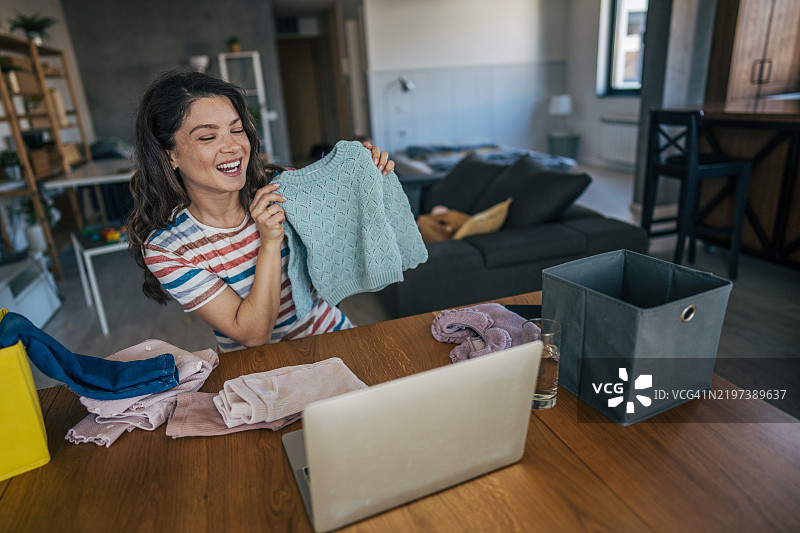 母亲坐在光线明亮的房间里，微笑着在笔记本电脑前展示她为小女儿购买的物品。图片素材