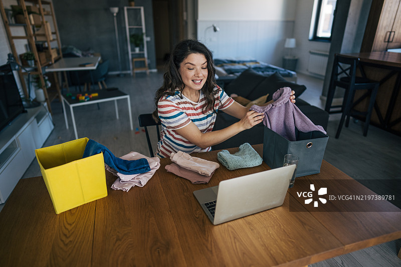 母亲坐在光线明亮的房间里，微笑着在笔记本电脑前展示她为小女儿购买的物品。图片素材