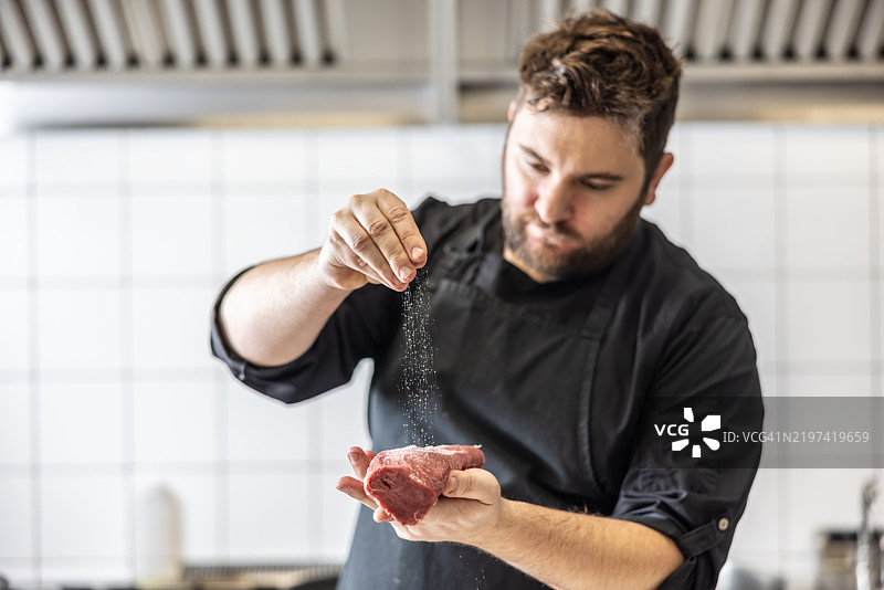 厨师在商业厨房中用盐和胡椒调味牛排。正在准备威灵顿牛肉。图片素材