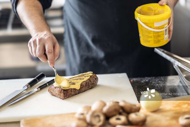 厨师在准备威灵顿牛肉时，将芥末涂抹在预先烹饪的牛排上。图片素材