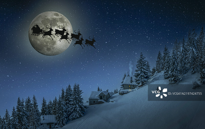圣诞老人雪橇的剪影在月光下飞向被雪覆盖的房子。图片素材