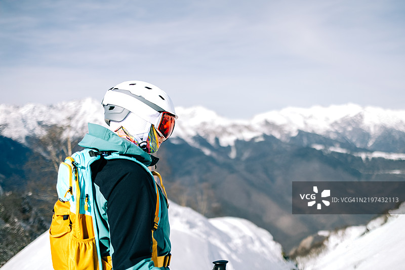 戴着头盔和背包的滑雪者在阳光明媚的日子里凝视着雪山峰。图片素材