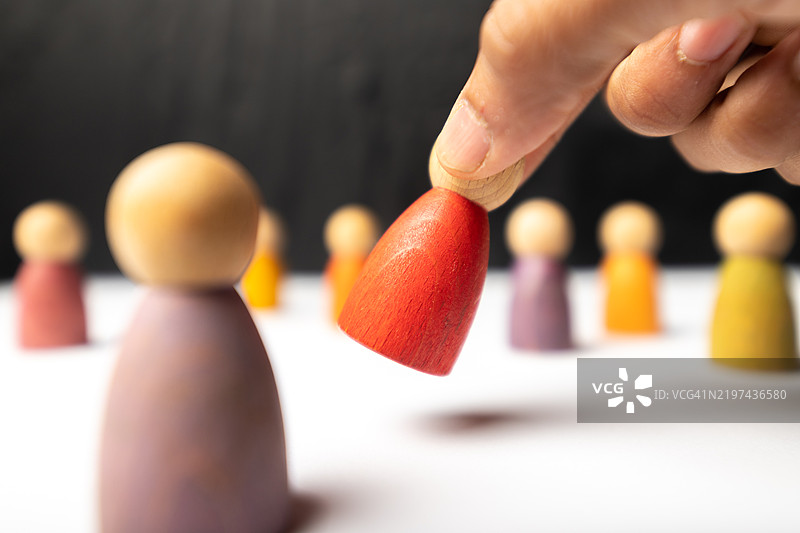 手将一个红色木制小雕像放置在其他雕像中间图片素材