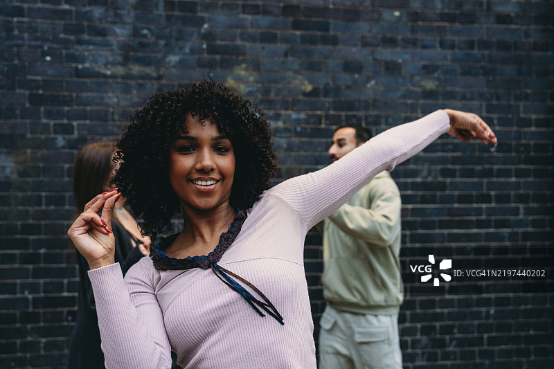 年轻女性与朋友在砖墙前跳舞图片素材