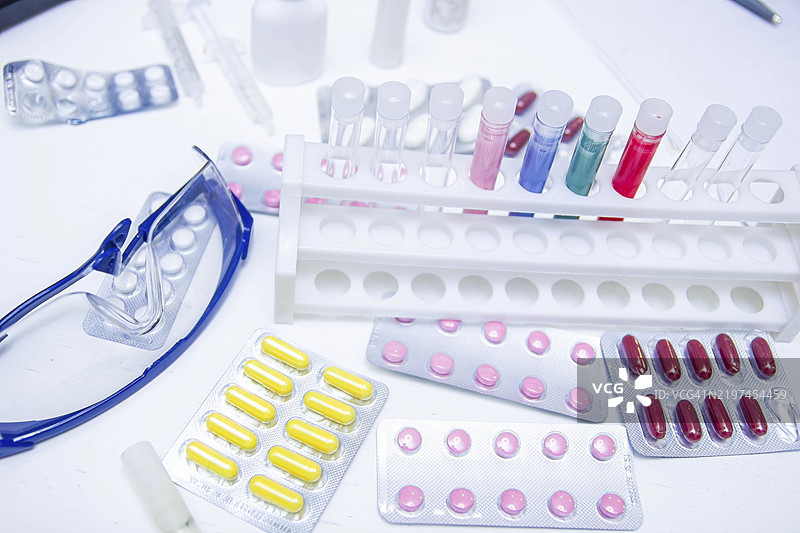 实验台上摆放着各种颜色的药丸和试管，旁边有安全眼镜图片素材