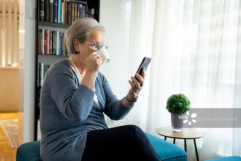 老年女性一边喝咖啡，一边使用手机和平板进行电子银行和在线学习图片素材