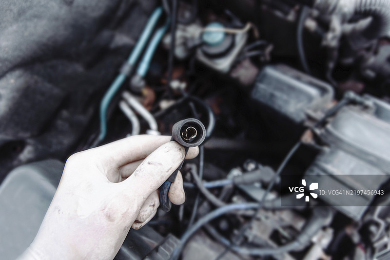 戴手套的手握着电气连接器，周围是汽车发动机部件。图片素材