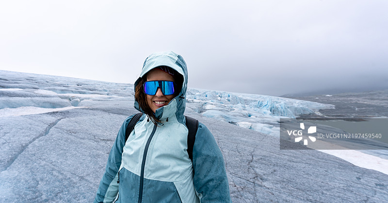 一位三十多岁的棕发女性，微笑着看向镜头，穿着登山装备。图片素材