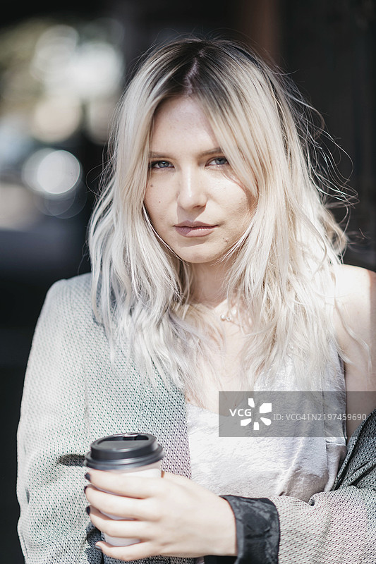 金发女性轻松地拿着咖啡杯，穿着休闲服，置身于柔和的光线环境中图片素材