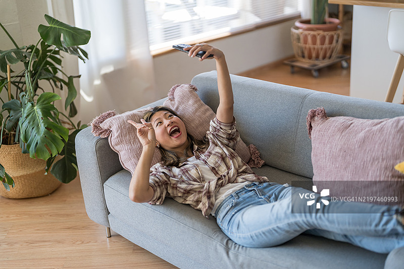 年轻女性躺在沙发上自拍并做出和平手势图片素材