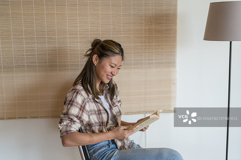 年轻女性在家中阅读一本书并微笑图片素材