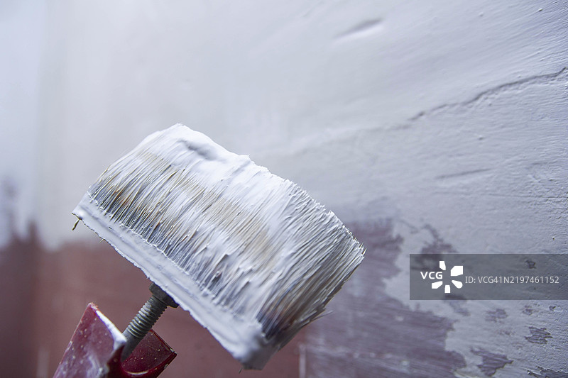 刷子近距离涂抹白色油漆，展示墙面上的纹理和刷痕图片素材