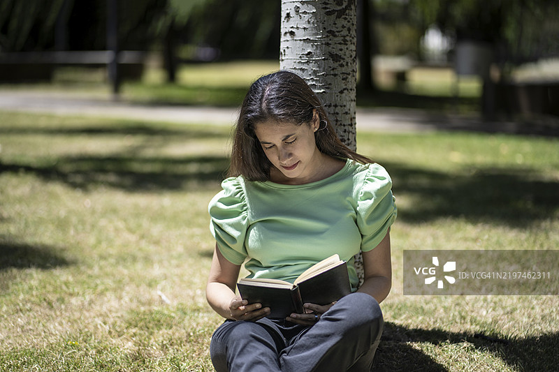 拉丁裔女性坐在树下阅读图片素材