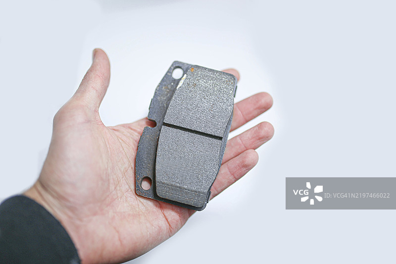 一个成年人手中握着单个刹车片，展示与手掌的大小对比图片素材