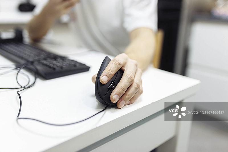 特写镜头：一只手在桌子上操作鼠标，旁边是键盘。图片素材