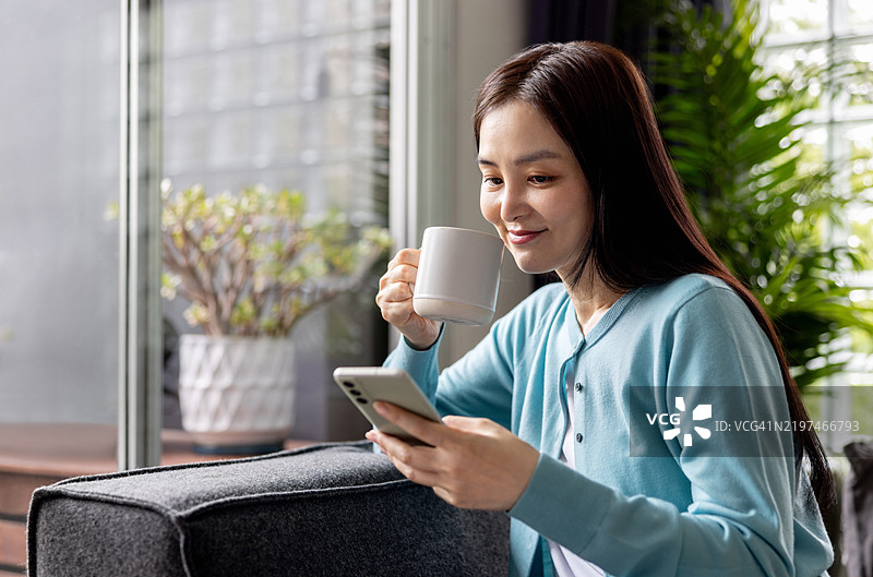 女人在家放松，喝着咖啡，同时用手机发信息图片素材