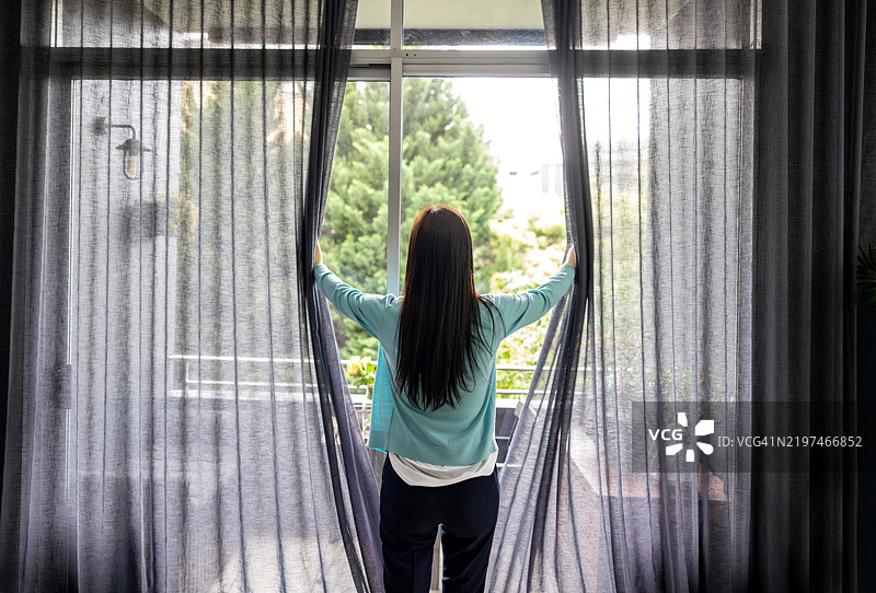 女人在家中拉开窗帘，欣赏窗外的景色图片素材