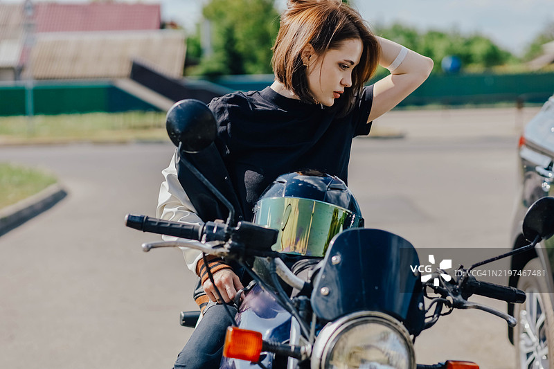 短发女性坐在阳光明媚的天空下停放的摩托车上图片素材